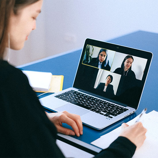 Image of woman at a laptop taking notes, laptop screen showing virtual meeting of three individuals